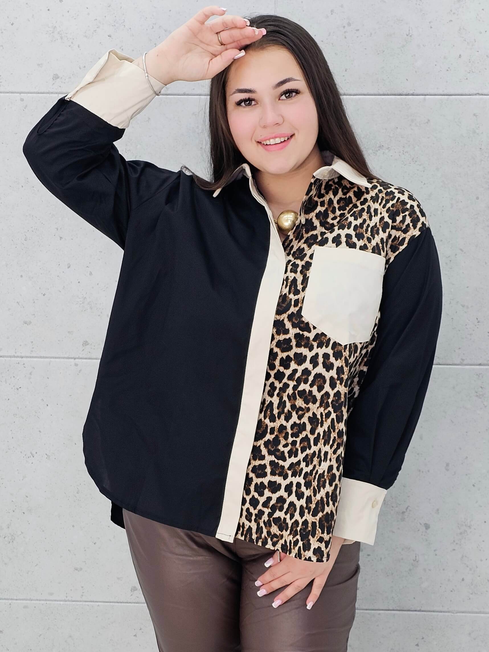 Modelka prezentuje czarno-beżową koszulę plus size z panterkowym wzorem . Koszula ma luźny krój, długi rękaw i kontrastowe wykończenia, idealna do stylizacji plus size.