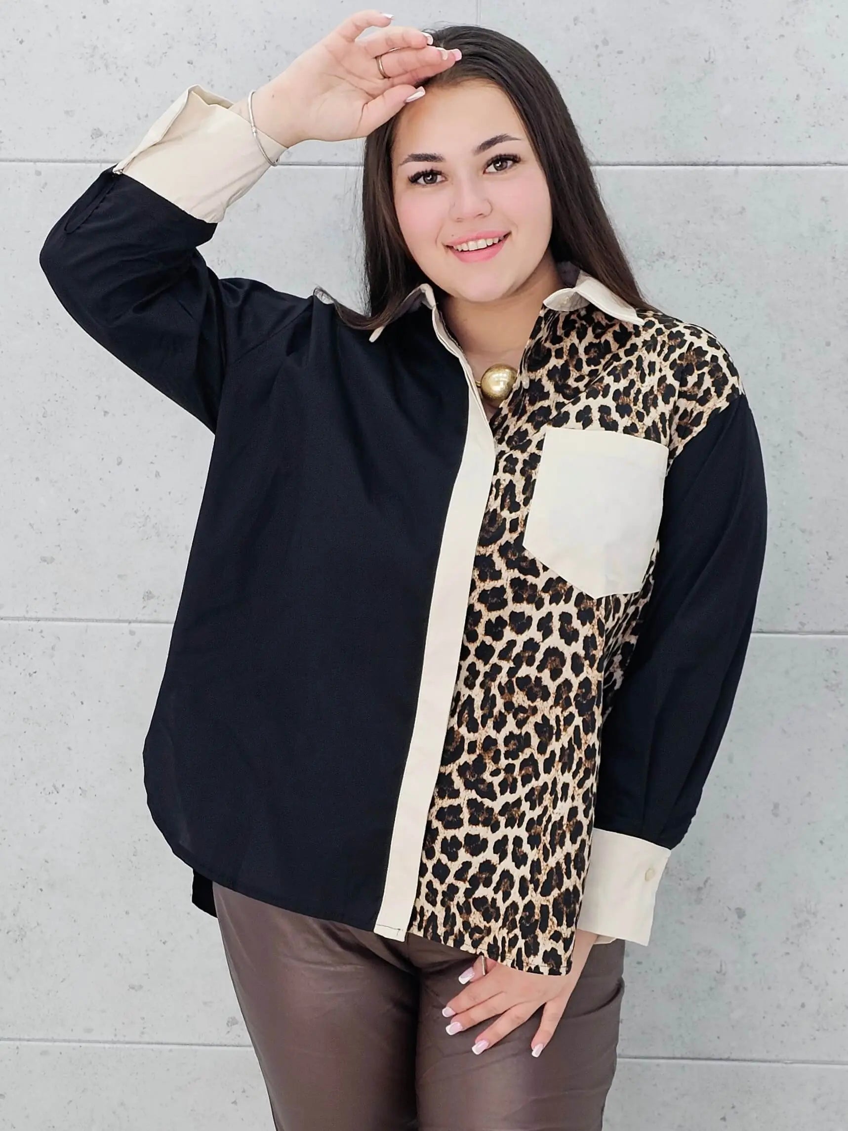 Modelka prezentuje czarno-beżową koszulę plus size z panterkowym wzorem . Koszula ma luźny krój, długi rękaw i kontrastowe wykończenia, idealna do stylizacji plus size.