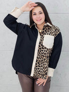 Modelka prezentuje czarno-beżową koszulę plus size z panterkowym wzorem . Koszula ma luźny krój, długi rękaw i kontrastowe wykończenia, idealna do stylizacji plus size.